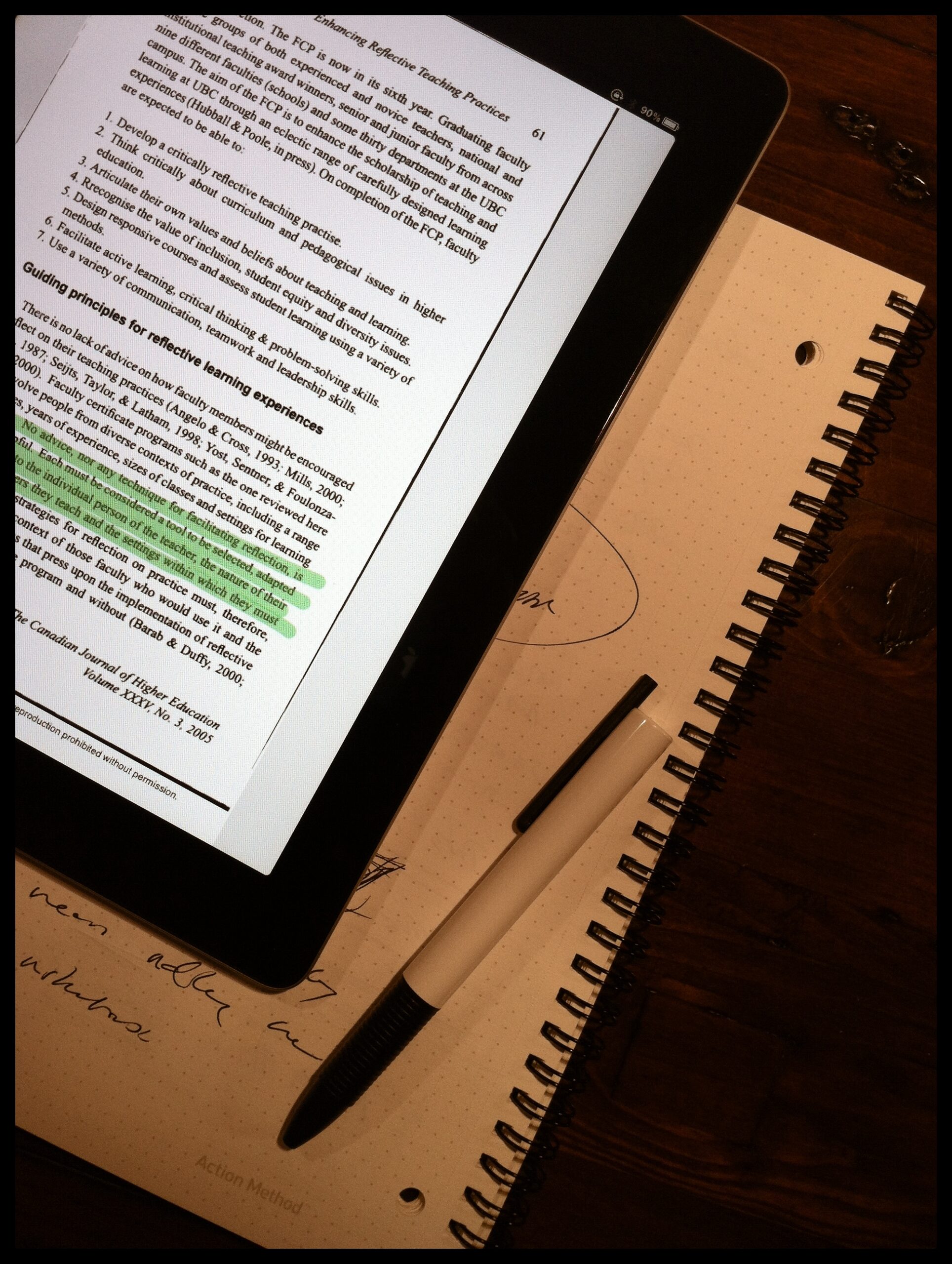 Electronic tablet, notebook, and pen on a desktop. Text on the tablet screen has been highlighted, notebook has some notes.